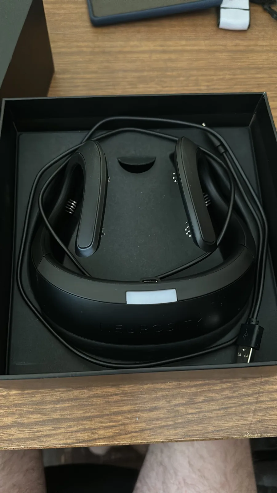 The Crown EEG headset resting in its box with its charging cable